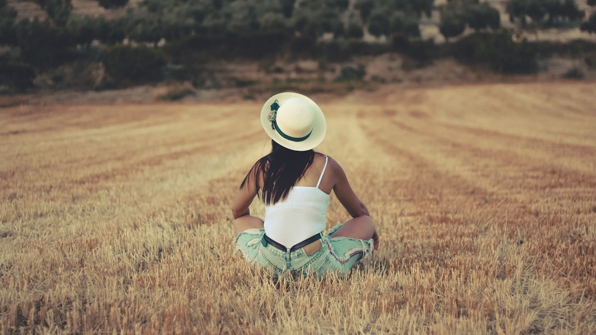 woman wearing white sunhat sitting on brown grassland during daytime